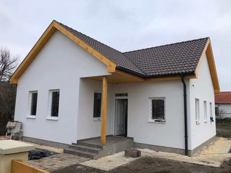 Elkészült, fehérre vakolt földszintes családi ház fa tornáccal